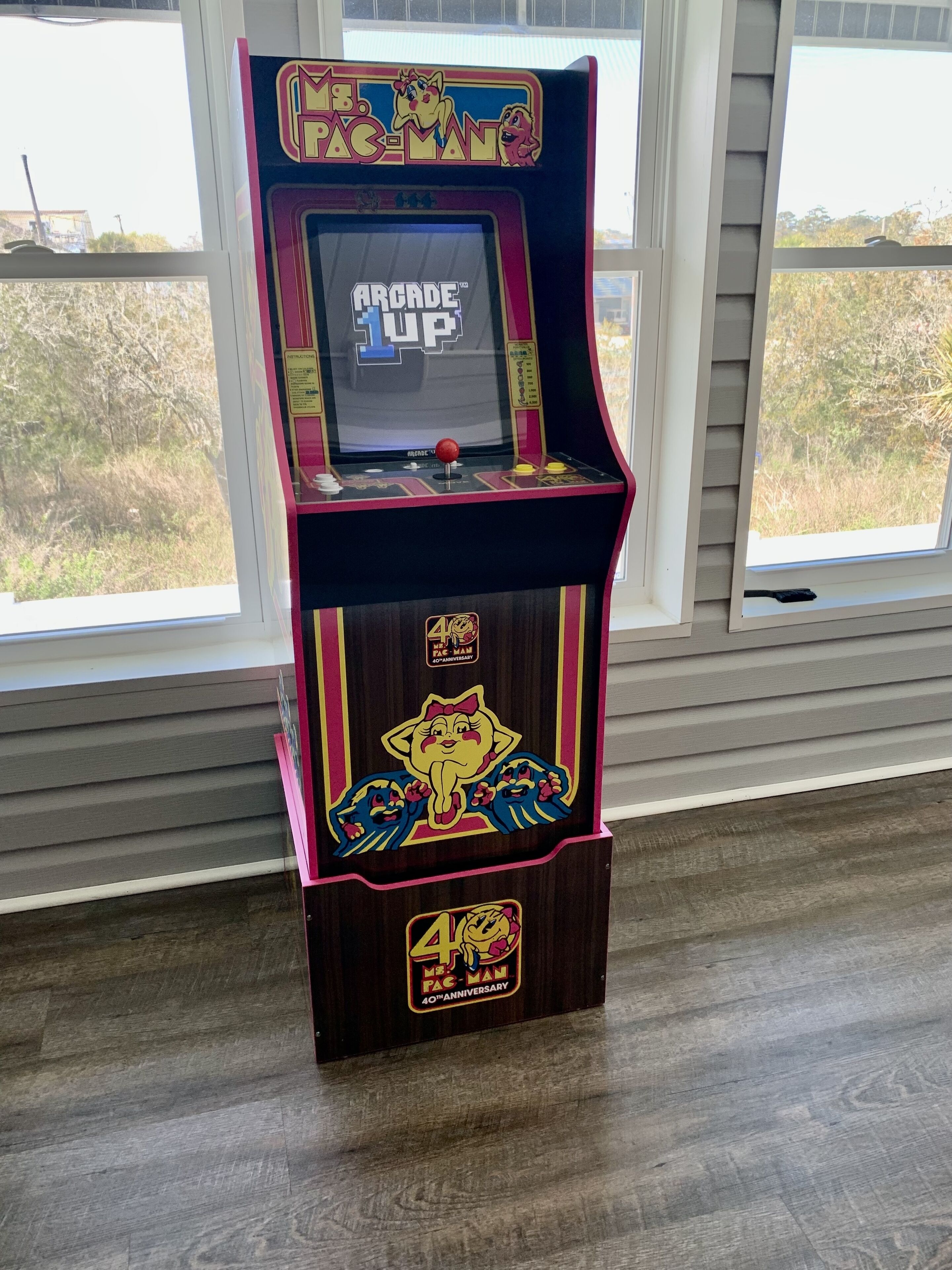 Una macchina arcade di Pac-Man con una targa celebrativa per il 40° anniversario, posizionata in interno vicino alle finestre.