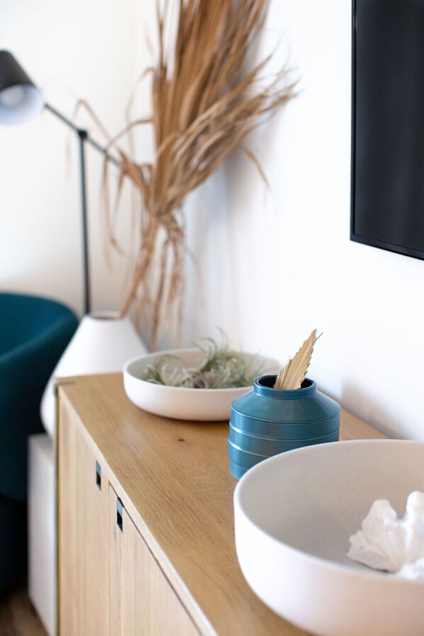 Una mesita de madera con un cuenco blanco, un florero azul con una planta y un cuenco blanco con un objeto blanco.