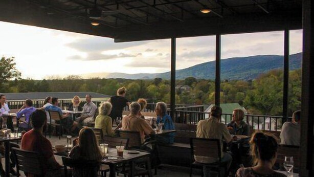 An outdoor dining area with tables and chairs, overlooking a mountainous landscape. - Piedmont Place 304 | Walkable to Downtown Crozet (Crozet)