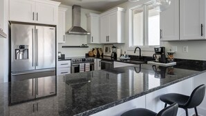 A modern kitchen with white cabinets, stainless steel appliances, a granite countertop, and pendant lighting. - Piedmont Place 304 | Walkable to Downtown Crozet (Crozet)