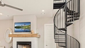 A modern living room with a fireplace, a white sofa, a striped rug, and a black spiral staircase. - The Dogwood - Hot Tub - Lake Front Access (Springdale)