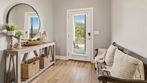 A hallway with a wooden console table, wicker baskets, a mirror, and a bench with patterned cushions. - The Dogwood - Hot Tub - Lake Front Access (Springdale)