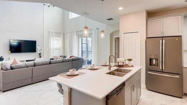 A modern kitchen with a central island, stainless steel appliances, and a grey sofa in the living area. - Luxury 5BR Family Oasis with Private Pool - 13 Guests (Kissimmee)