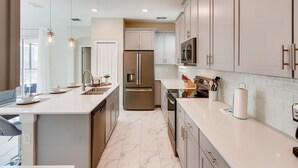 A modern kitchen with a central island, stainless steel appliances, and light-colored cabinetry. - Luxury 5BR Family Oasis with Private Pool - 13 Guests (Kissimmee)