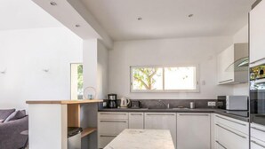 Une cuisine moderne avec des meubles blancs, un plan de travail en marbre et un coin repas comprenant une table et des chaises.