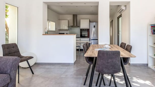 Une cuisine moderne avec des meubles blancs, un îlot central et un coin repas comprenant une table et des chaises en bois.