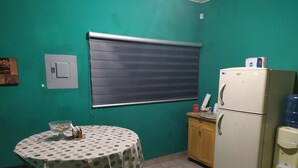 Una piccola cucina con un tavolo ricoperto da una tovaglia a pois, un frigorifero, un dispenser d'acqua e una finestra con una tenda.