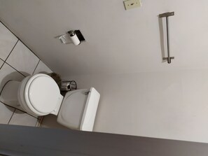 A standard bathroom with a toilet, trash bin, and toilet paper holder.