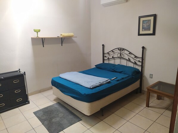 A bedroom with a bed, a bedside table, a dresser, a shelf with a vase, and a framed picture on the wall. - Cuarto Comodo Centrico (Mexicali)