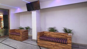 A lobby area with two wooden benches with cushions, a flat-screen TV mounted on the wall, and potted plants. - OYO 10321 Koramangala (Bengaluru)