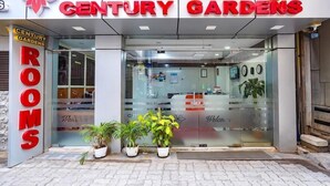 The exterior of Century Gardens with a glass entrance, potted plants, and a sign indicating rooms. - OYO 10321 Koramangala (Bengaluru)