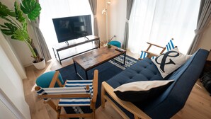 Una sala de estar con un sofá, sillones a rayas, una mesa de centro, un televisor y una planta grande.