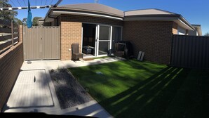 A backyard with a paved patio, a lawn, a brick wall, and a wooden fence. - JoyWaves New  4Bedroom retreat - ultimate getaway
 (Kambah)