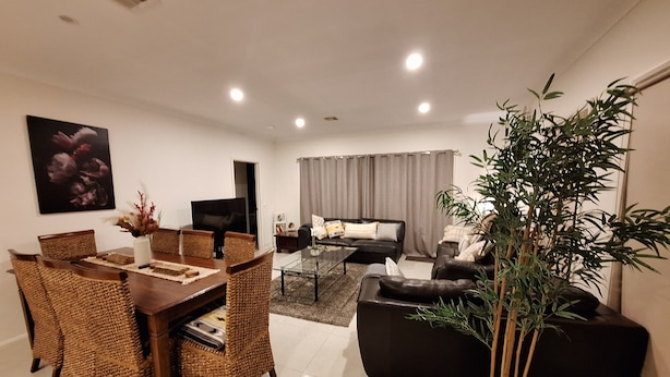 A modern living room with a dining area, a sofa, a coffee table, and a large potted plant. - JoyWaves New  4Bedroom retreat - ultimate getaway
 (Kambah)