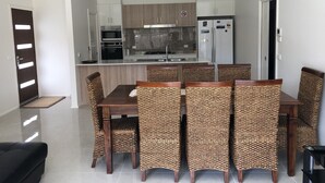 A modern kitchen with built-in appliances, a dining area with wicker chairs, and a black sofa. - JoyWaves New  4Bedroom retreat - ultimate getaway
 (Kambah)
