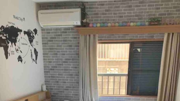 Un dormitorio con pared de ladrillo, un mapa del mundo, una cama, una ventana con cortinas y un balcón pequeño.