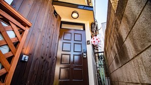 A wooden door with a small porch area, a metal gate, and a stone wall. - A0 Shinjuku Big House (Tokyo)