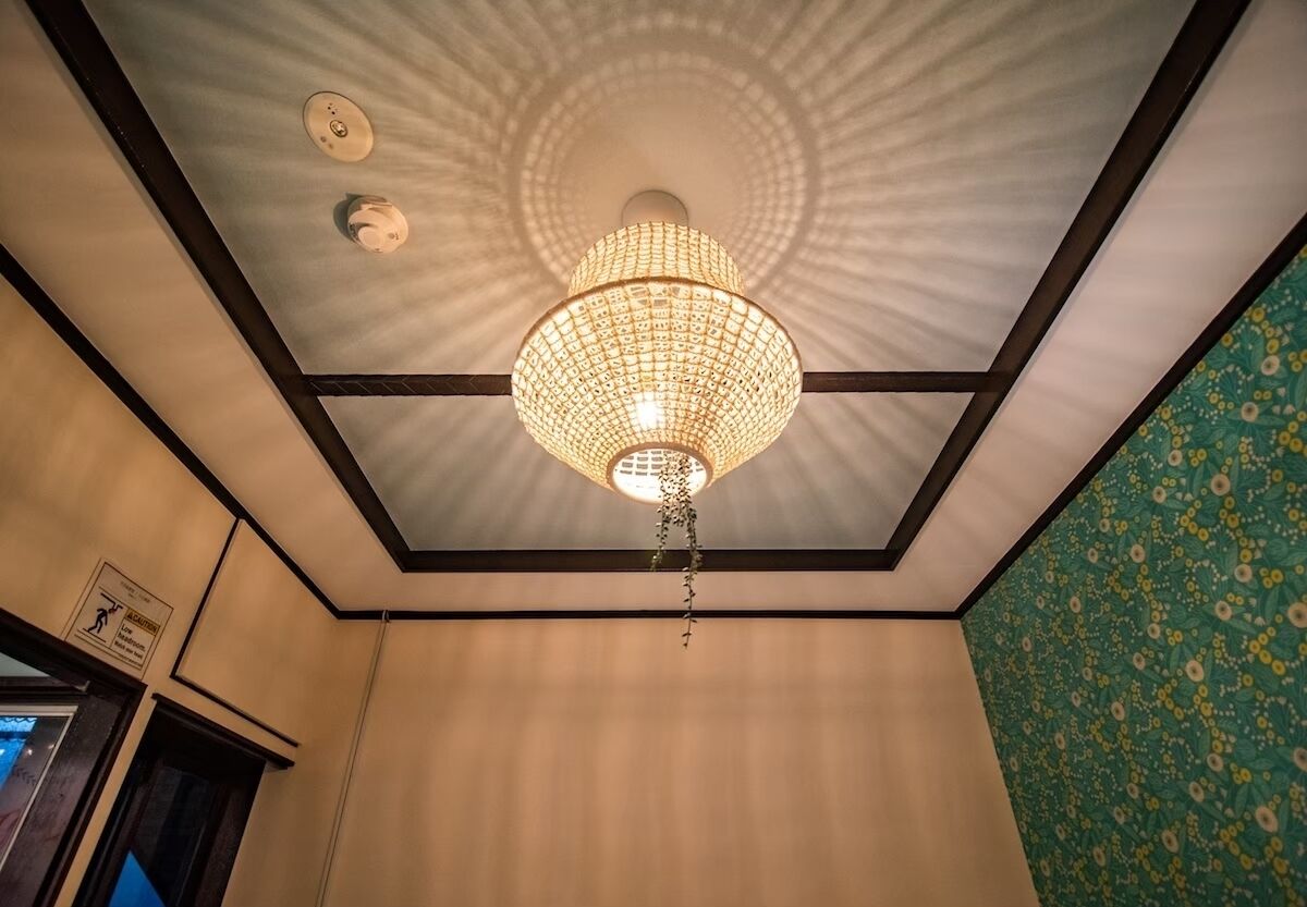 A room with a patterned ceiling, a hanging light fixture, and a floral wallpaper on one wall.
