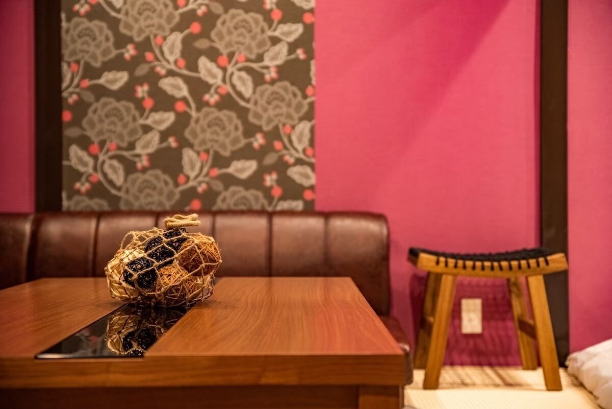 Una mesa de madera con una cesta tejida y un teléfono inteligente. Un taburete de madera pequeño está al lado de la mesa.