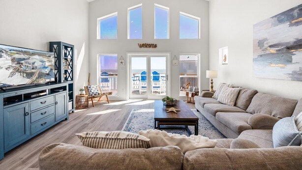 A spacious living room with a large TV, a sofa, and a coffee table. There is a view of the outside through large windows. - Private Heated Pool, walkout on the beach! - Island Star (Dauphin Island)