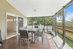 A covered patio with a table and chairs, a sliding glass door, and a view of a backyard with a fence and trees.
