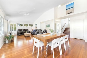 A spacious living area with a wooden dining table and white chairs, a leather sofa, and a ceiling fan.