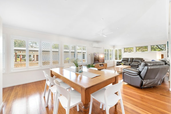 A spacious living area with a wooden dining table, white chairs, and a leather sofa.