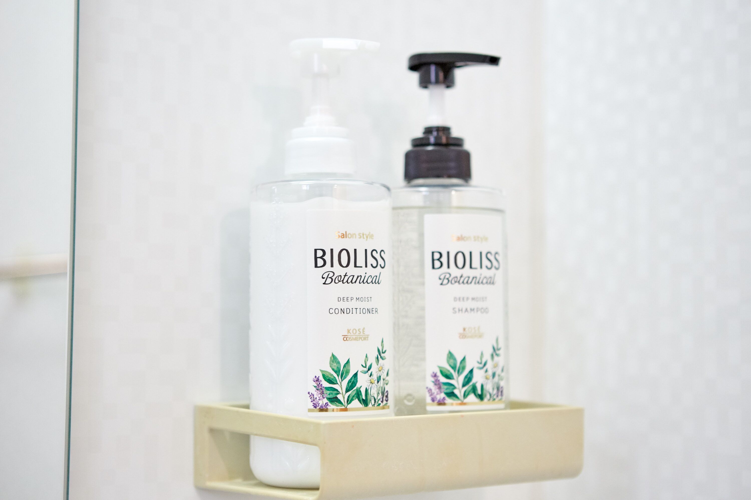 Two bottles of Bioliss Botanical deep moisture conditioner and shampoo on a white shelf.