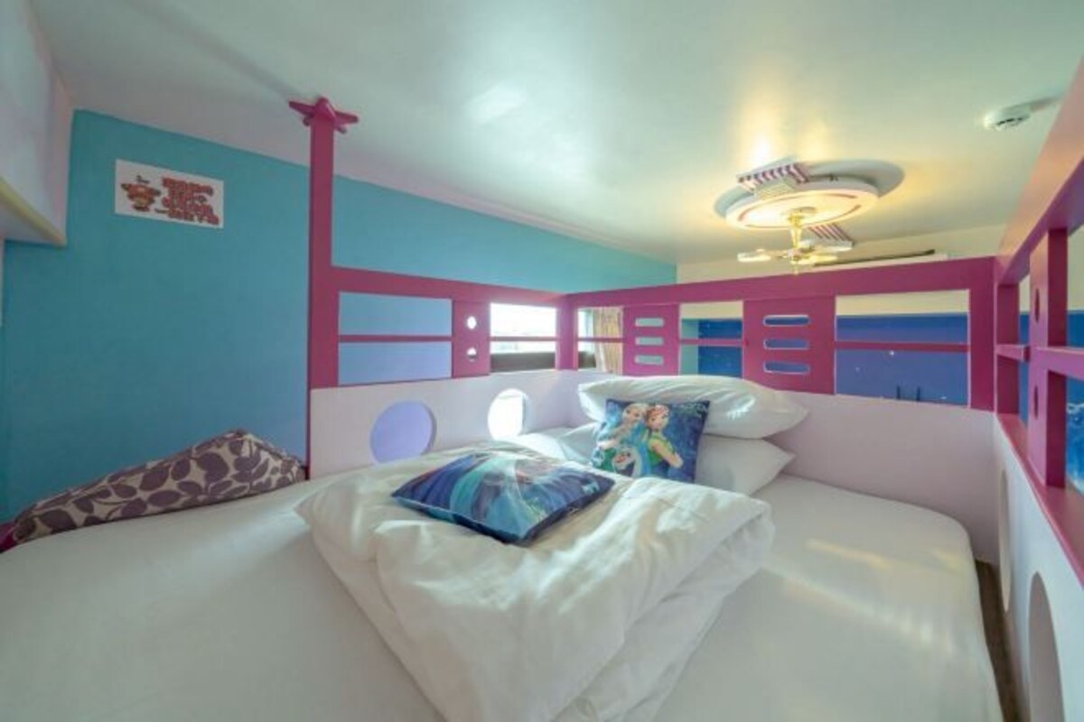 Una camera da letto con un letto, cuscini, una ventola a soffitto e una parete con un cartello.