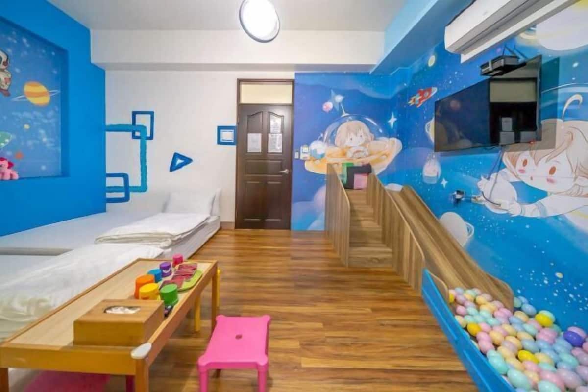 Kinderzimmer mit Bett, Spieltisch, rosa Hocker, Bällebad und Wandgemälde einer im Weltraum schwebenden Mädchen.