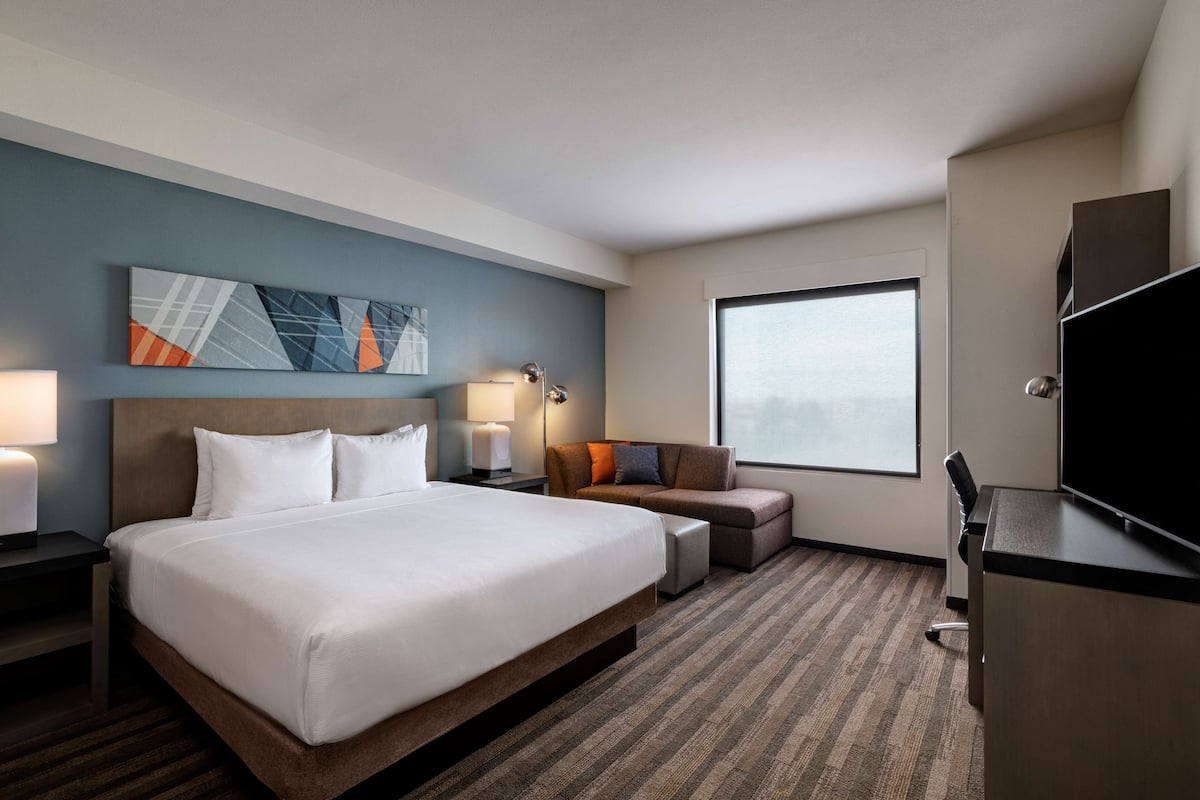 A hotel room with a large bed, a desk, a chair, a sofa, and a TV.