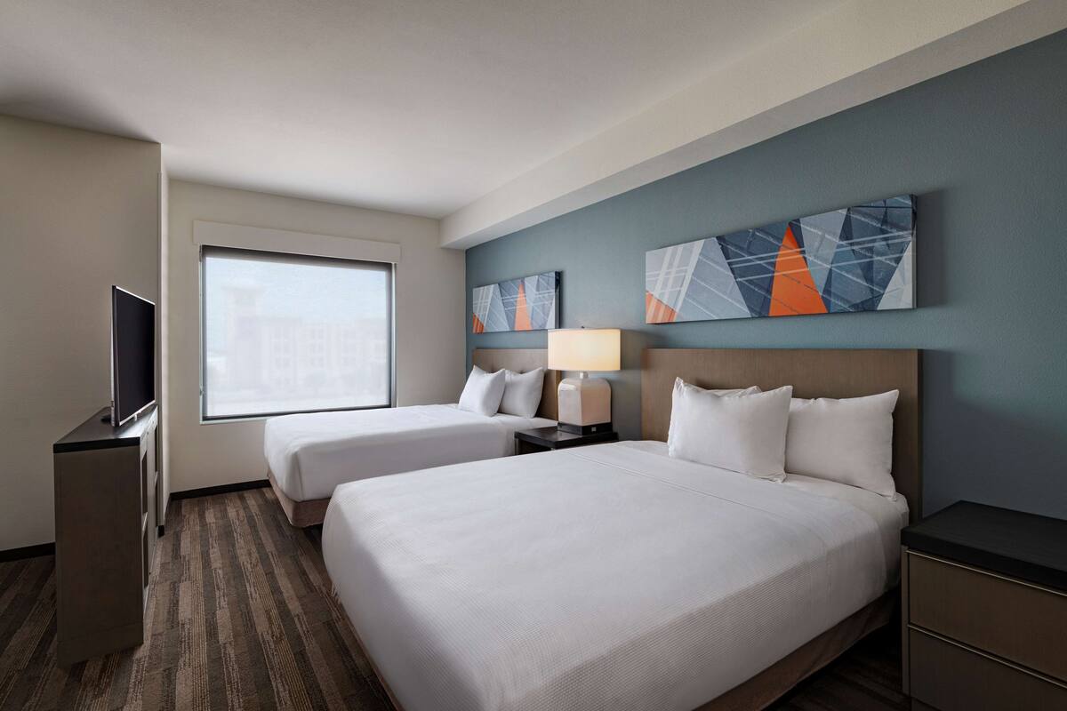 A hotel room with two beds, a TV, a desk, and artwork on the wall.
