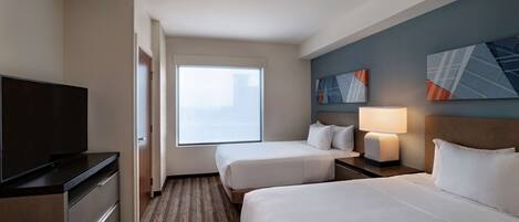 A hotel room with two beds, a TV, a desk, and a window.