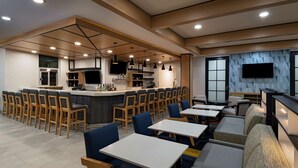Un restaurante moderno con área de bar, disposición de mesas y cocina al fondo.