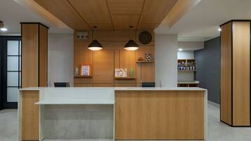 A reception desk with a wooden finish, two pendant lights, a bulletin board, and a bookshelf with various items.