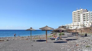 A beach with thatched umbrellas, a rocky shoreline, and a high-rise hotel in the background.