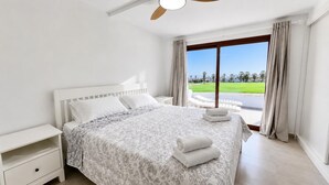 A bedroom with a bed, nightstand, and a view of a green landscape through a large window. - Sunset Horizon, Golf del Sur (San Miguel de Abona, Golf del Sur)