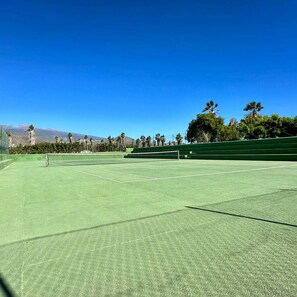 A tennis court with a net, surrounded by trees and a clear blue sky.