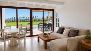 Una sala de estar con sofá, mesa de centro y sillones, con un ventanal corredizo que da a un patio con mobiliario exterior.