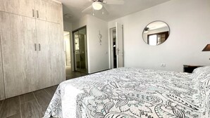 A bedroom with a bed, a ceiling fan, a wardrobe, and a bathroom visible through an open door.