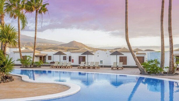 A swimming pool with lounge chairs and palm trees, surrounded by white buildings with tiled roofs. - Summer House, Golf del Sur (San Miguel de Abona, Golf del Sur)