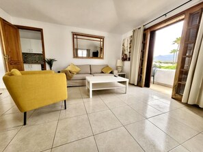 A living room with a sofa, a yellow armchair, a white coffee table, a large mirror, and a view through a sliding door.