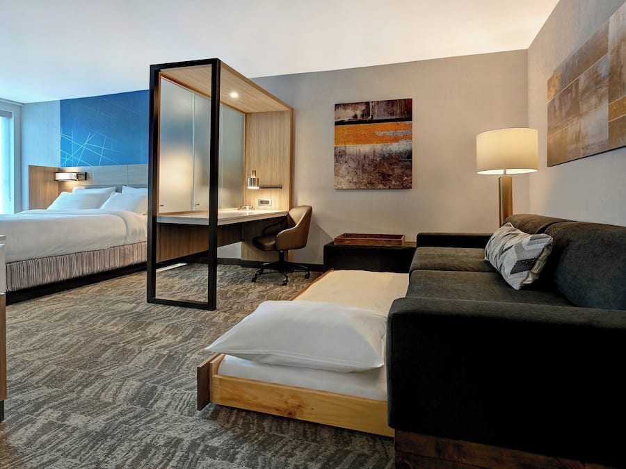 A hotel room with a bed, a desk, a chair, a sofa, and a large mirror.