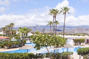 Ett poolområde vid ett semesterhotell med palmer, klar himmel och berg i bakgrunden.