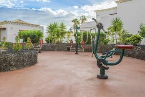 Outdoor exercise equipment, a paved area, and surrounding greenery.