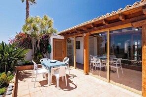 Une terrasse avec une table et des chaises, une pergola en bois et une porte vitrée donnant sur un espace intérieur.