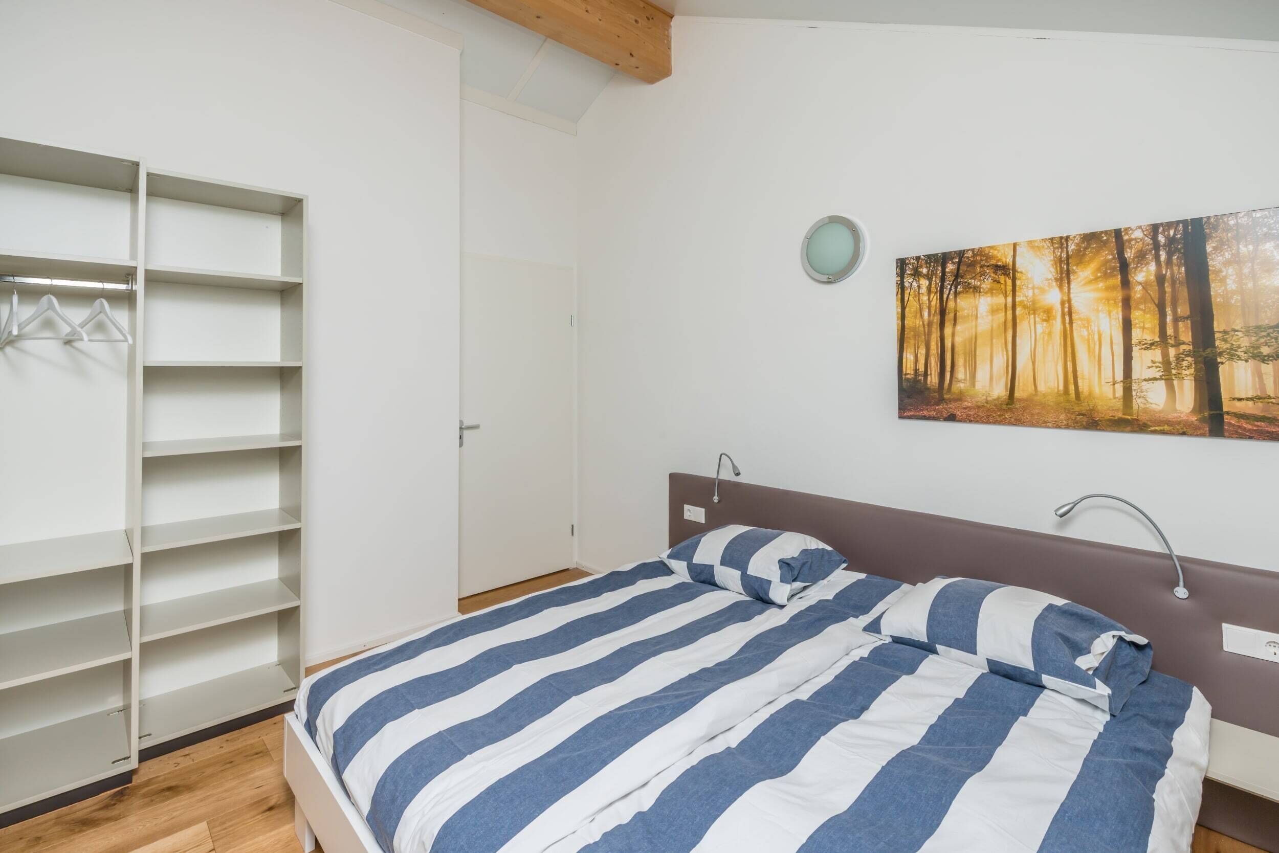 A bedroom with a bed, a wardrobe, and a wall-mounted picture of a forest.