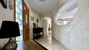 Un couloir avec une porte en bois, une lampe noire, une console et un sol carrelé.