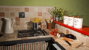 A kitchen with a gas stove, a pot of spaghetti, fresh tomatoes, and a cutting board with vegetables.