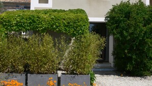 Una casa de dos pisos con techo inclinado, una ventana pequeña con contraventanas y un camino de entrada de grava.